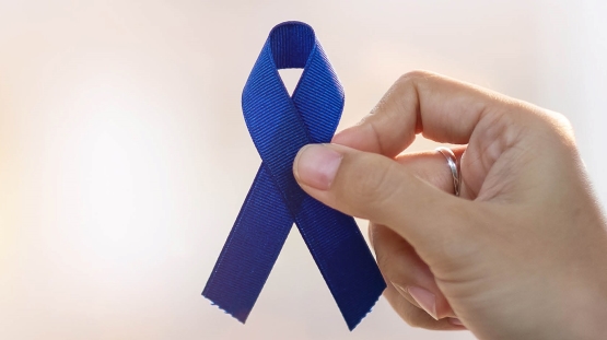 Hand holding dark blue ribbon to support colorectcal cancer awareness month