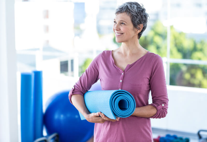 Woman smiling holding yoga mat